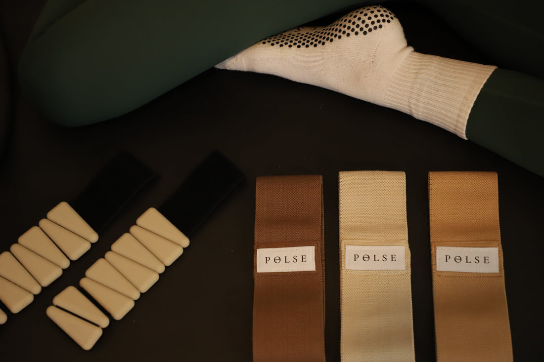 Pilates essentials including grip socks, a workout mat, booty bands, and ankle weights arranged for a home or studio workout